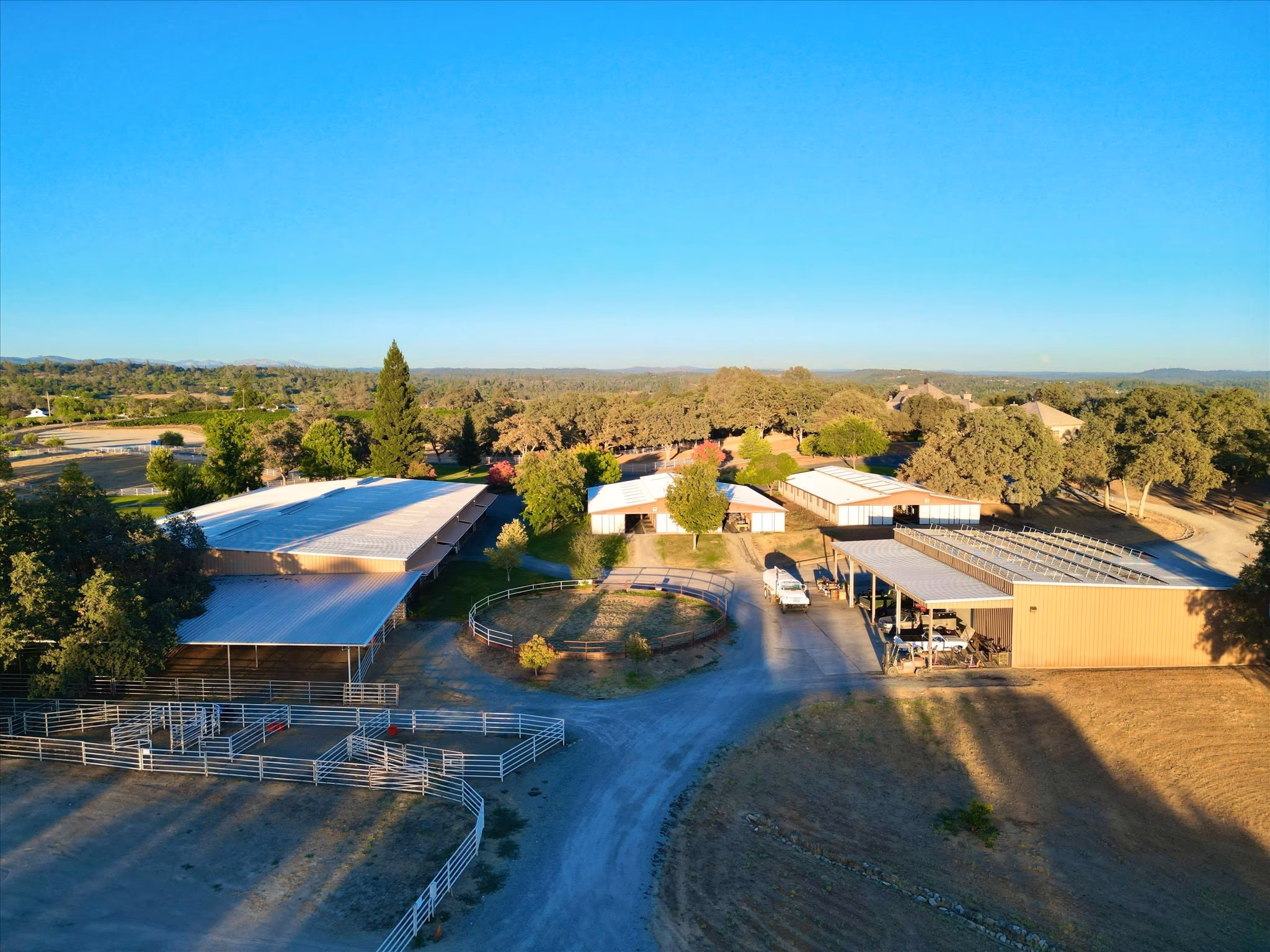 The equestrian facility from the air: the covered arena roof, the barns and the surrounding paddocks.