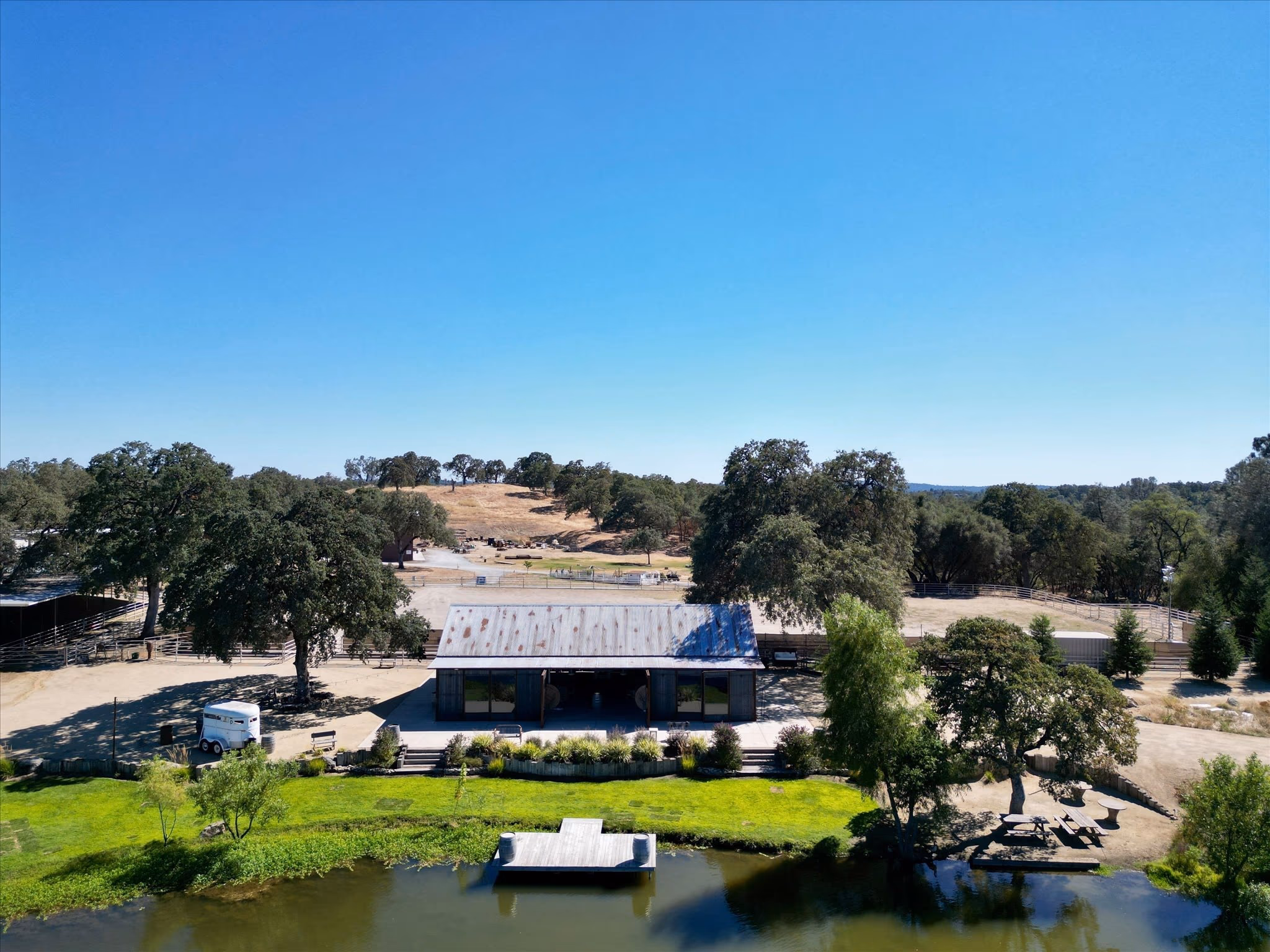 The event barn seen across the lawn and the water, with mature oaks and the ranch beyond.