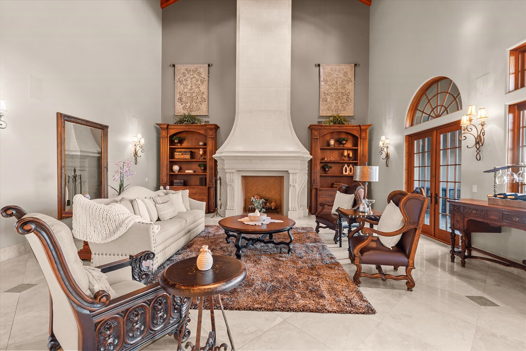 The great room of the main residence, with a full-height carved limestone fireplace, an exposed timber cathedral ceiling and French doors along one wall.