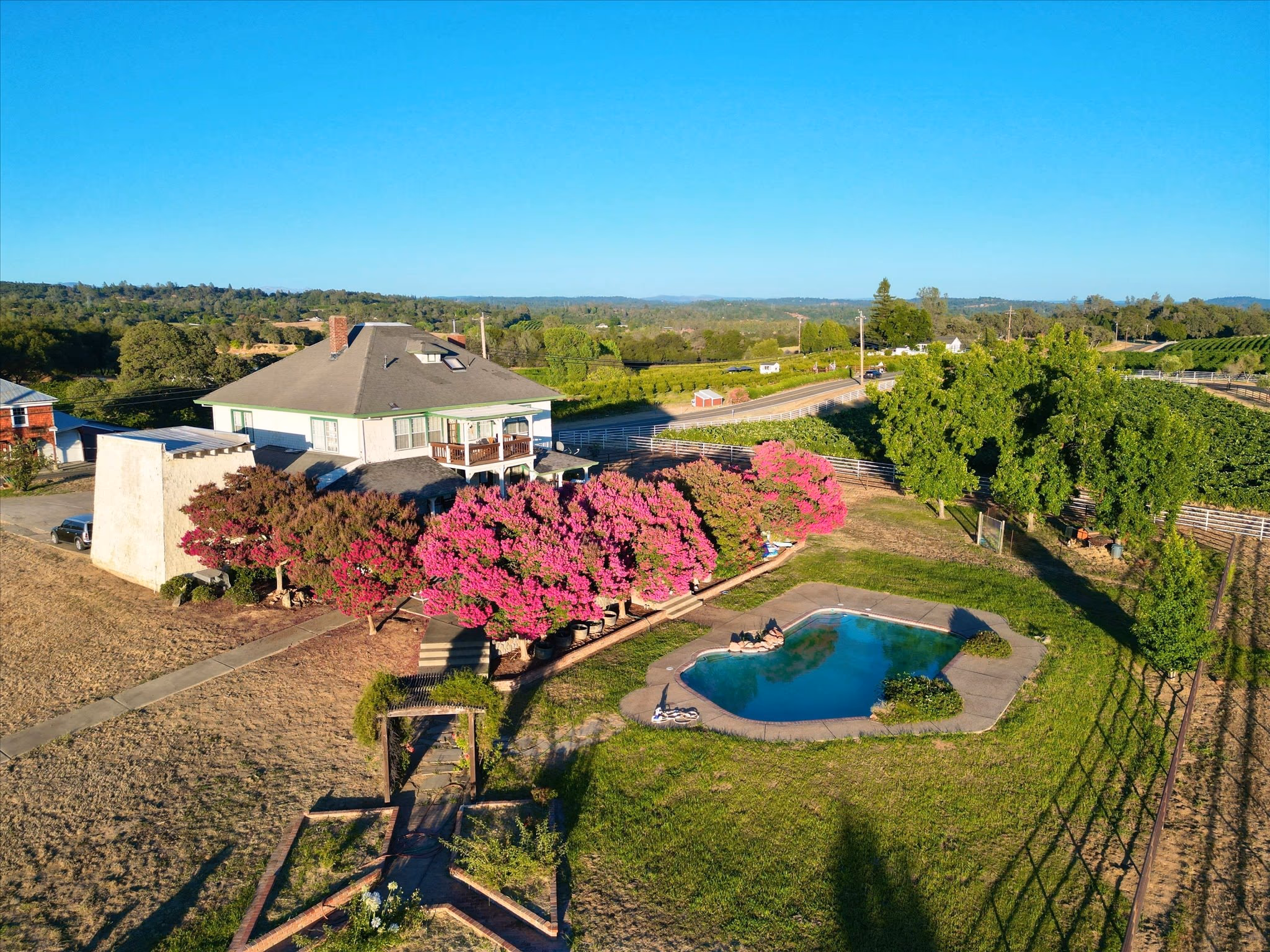 The restored historic home from the air, a two-story house with a wraparound porch, flowering crepe myrtles and a swimming pool, with vineyard rows behind.