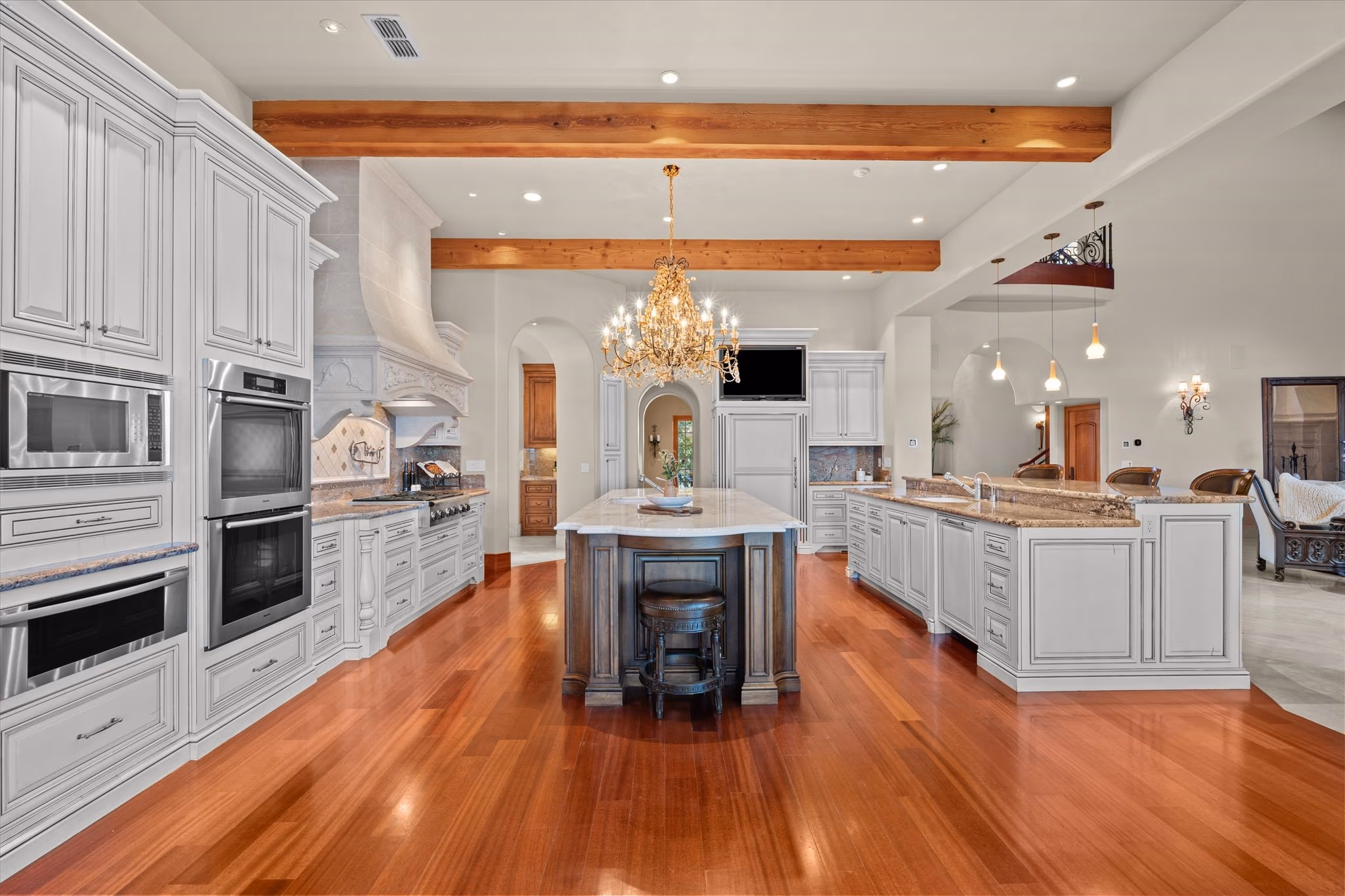 The kitchen of the main residence, with two islands, a chandelier, exposed beams, cherry floors and painted cabinetry.