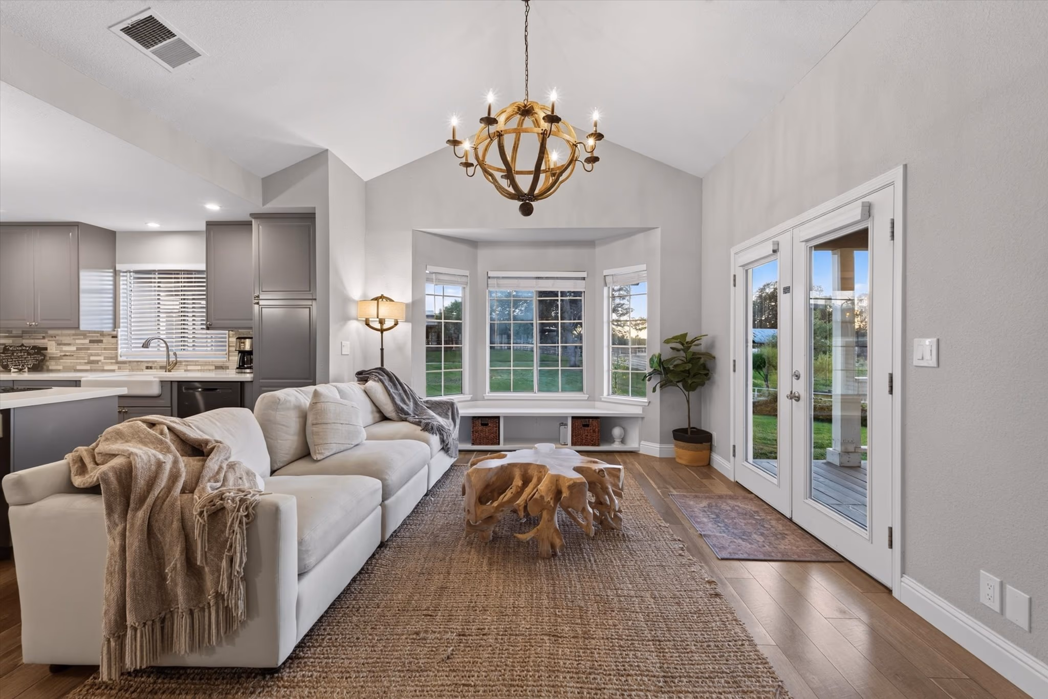 The living room of the lake house, with a vaulted ceiling, a chandelier, a bay window and French doors to the lawn.